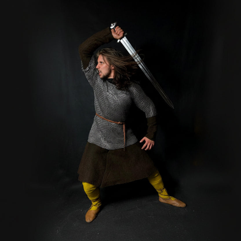 Person in chainmail holding a sword against a dark background